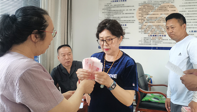 頭題片，5月30日，某藥業(yè)公司按協(xié)議約定完成第一期履行義務(wù)，將十萬現(xiàn)金交到法院，調(diào)解員付菊（左一）清點(diǎn)無誤之后交到農(nóng)民工委托代理人徐某手中